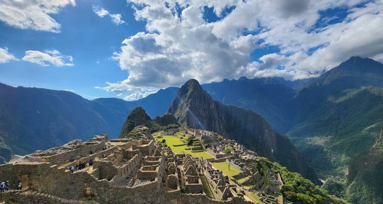 Luchtfoto van Machu Picchu's stenen structuren en terrassen verlicht door de middagzon tegen ruige bergtoppen.