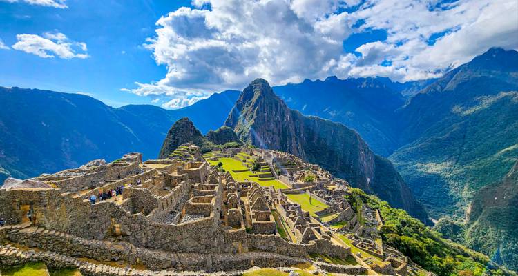 Kristalhelder panorama van de ruïnes van Machu Picchu badend in het felle zonlicht onder dramatische wolken en bergtoppen.