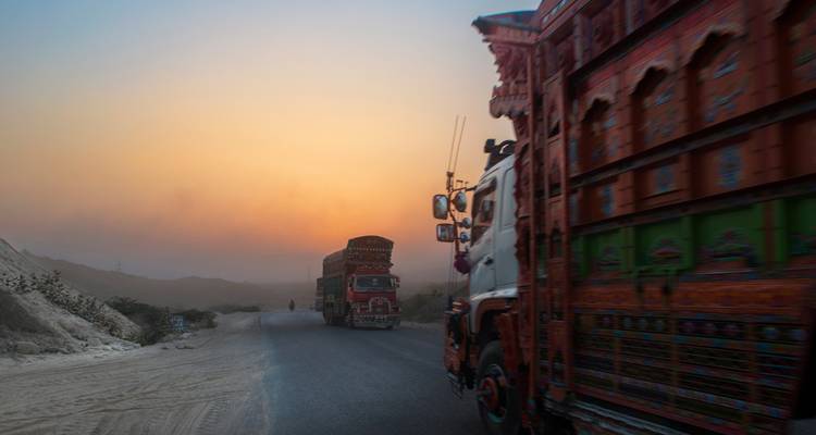 Des camions pakistanais richement décorés roulant le long d'une route poussiéreuse au coucher de soleil coloré.