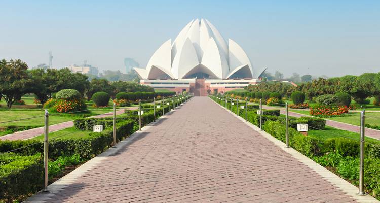 Long brick walkway flanked by manicured gardens leading to the white Lotus Temple’s striking petal-shaped architecture.