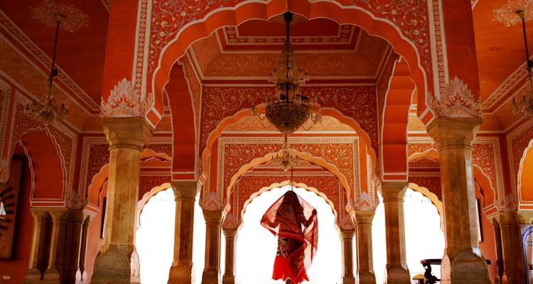 Intricately painted arches of Jaipur’s City Palace with a lone draped figure beneath a chandelier.