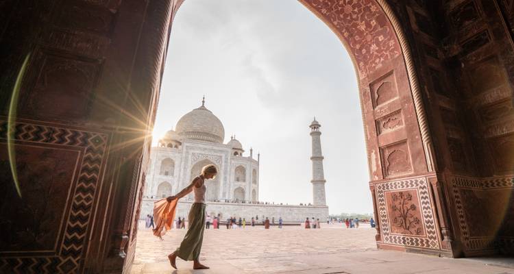 Traveler framed by an ornate red archway gazing at the Taj Mahal bathed in soft sunlight.