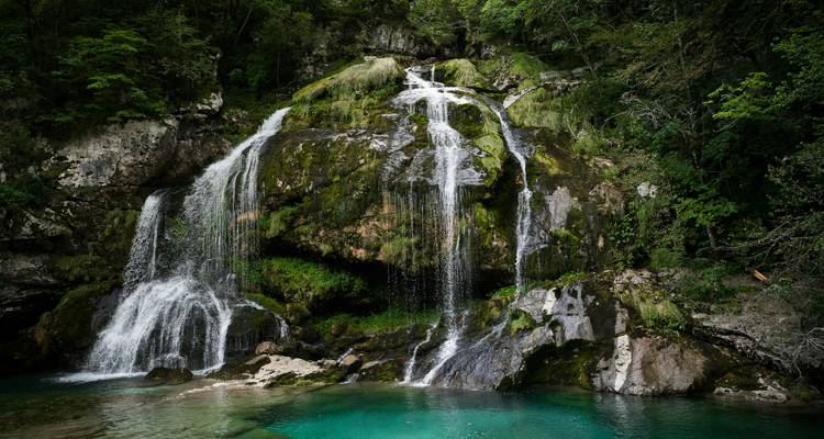 Kristallklares türkisfarbenes Becken und stufenweise Wasserfall umgeben von üppigem slowenischem Wald