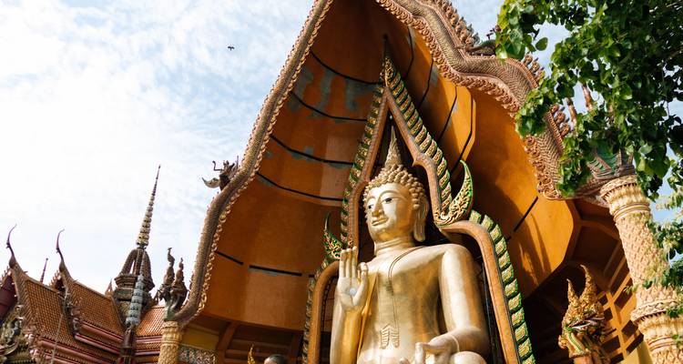 Golden Buddha and ornate temple roofs of Wat Tham Sua shine against a bright sky.