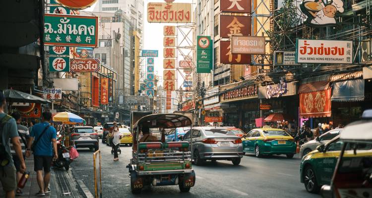 Vibrant Bangkok street lined with colorful signs, vehicles and bustling pedestrians.