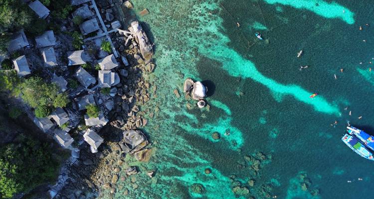 Aerial view of turquoise reef waters, rocky shoreline cottages and snorkelers.