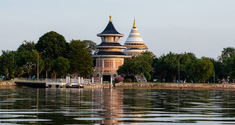 Decorative pagoda buildings reflected on a calm lake at golden hour.