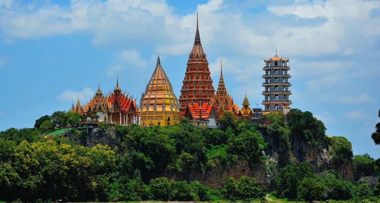 Colorful multi-tiered temple complex crowns a lush green hilltop under blue skies.