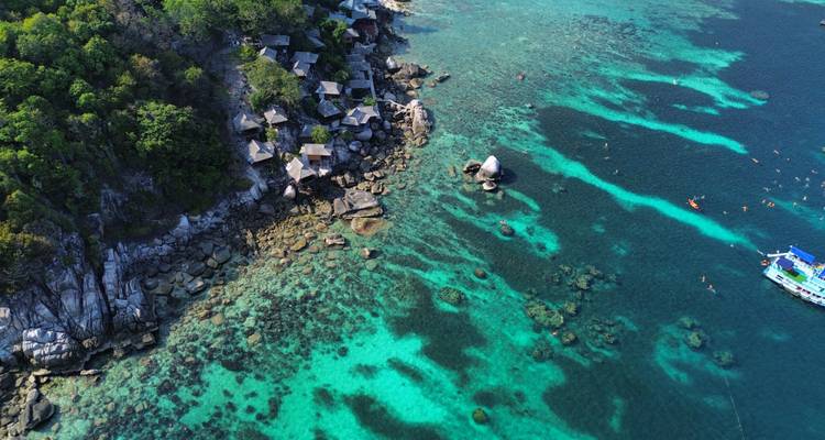 Drone image of vibrant turquoise reef waters and rocky coastline with scattered snorkelers.