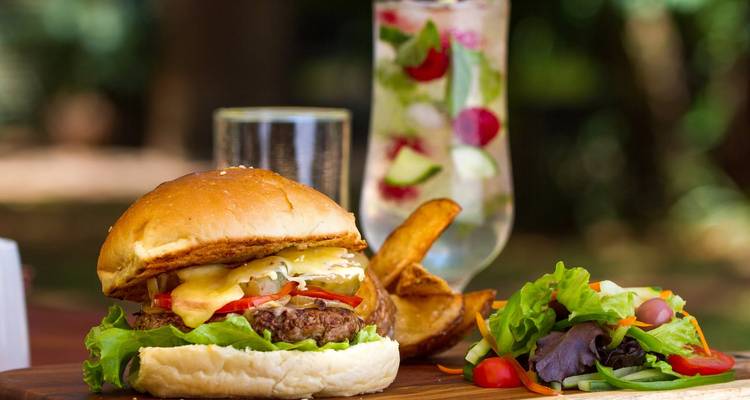 Gourmet-Cheeseburger mit Pommes, frischem Salat und Fruchtsaftgetränk auf Holztisch im Freien