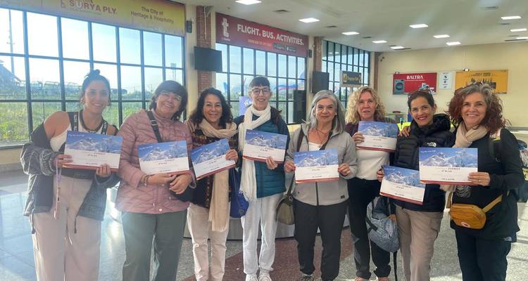 Group of women proudly holding mountain flight certificates inside a bright airport hall.