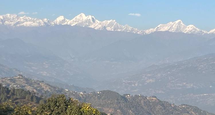 Clear view of distant snow-covered Himalayan peaks rising above layered foothills under a blue sky.
