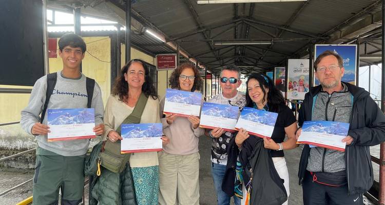 Six smiling travellers holding Everest flight certificates while posing together in an airport walkway.