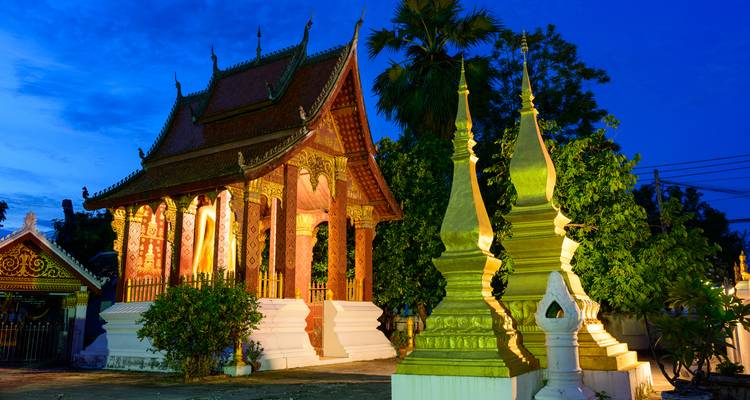Ein aufwendig gestalteter buddhistischer Tempel und vergoldete Stupas, wunderschön gegen einen tiefblauen Abendhimmel beleuchtet.