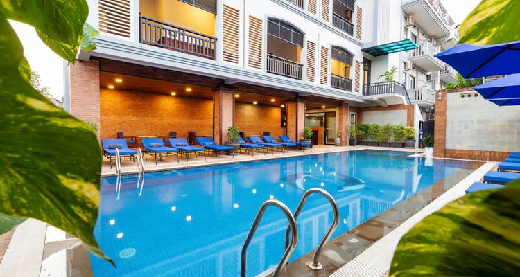 Einladendes Außenhotel-Schwimmbad, umgeben von blauen Liegestühlen und Blatterpflanzen.