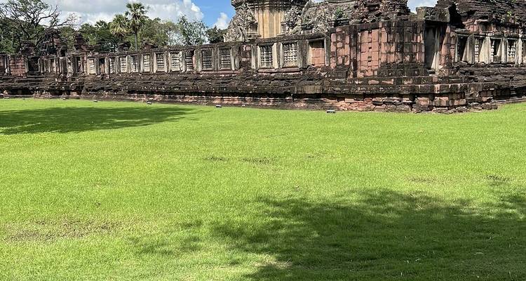 Side view of extended temple wall and windows set beyond a wide green lawn under partly cloudy sky.