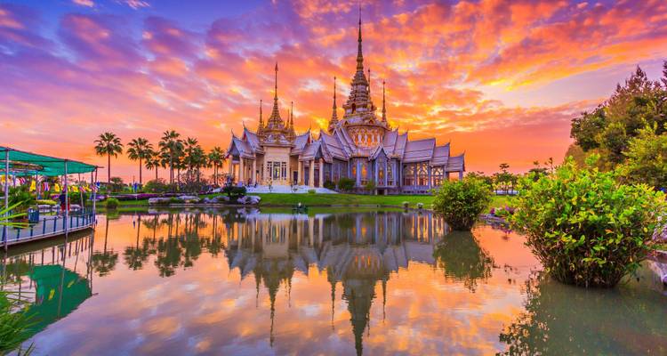 Ornate Thai temple mirrored in a tranquil pond at vibrant sunset with fiery clouds.