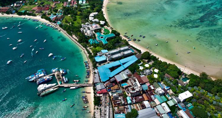Dramatic aerial of a turquoise bay, boats, resorts and coral shallows on a Thai island.