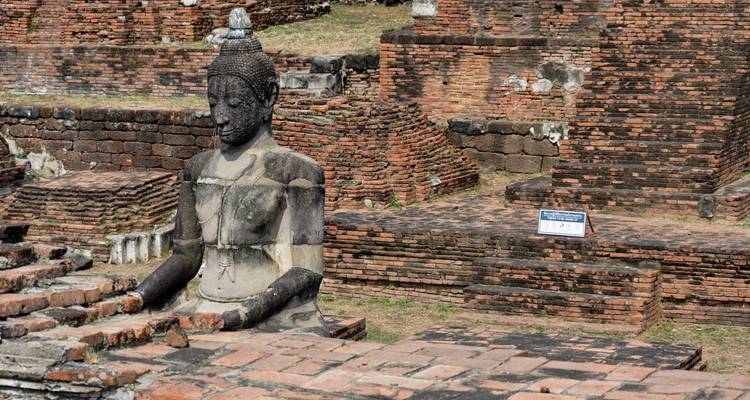 Weathered brick Buddha statue amid crumbling ruins of Sukhothai Historical Park.