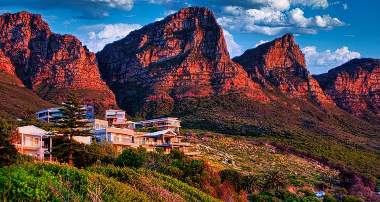 Modern homes nestle beneath the fiery red cliffs of the Twelve Apostles at sunset.