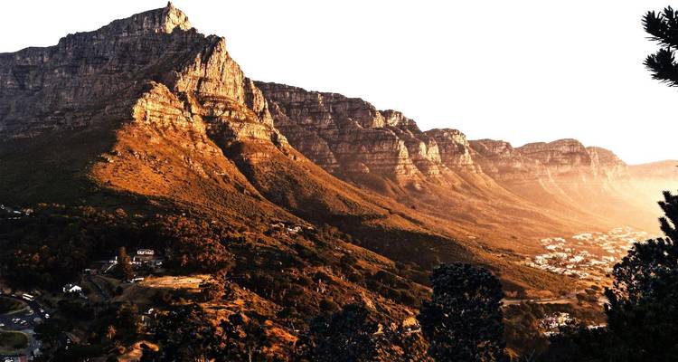 Side-lit Table Mountain massif rises above city foothills in warm evening light.
