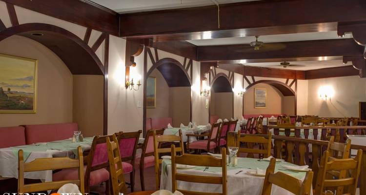 Sala de comedor de restaurante con iluminación tenue, vigas de madera y sillas con cojines rosa; texto de marca de agua en la esquina inferior.