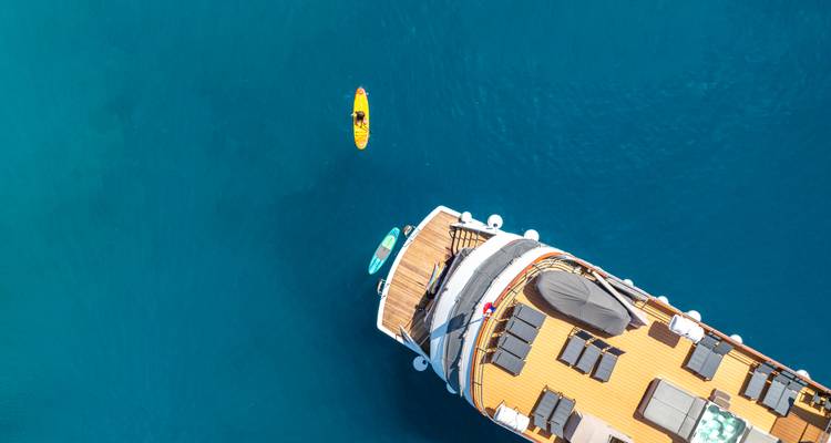 Toma aérea con drone de un yate con tumbonas y un kayak amarillo remando cerca en un mar azul cristalino.