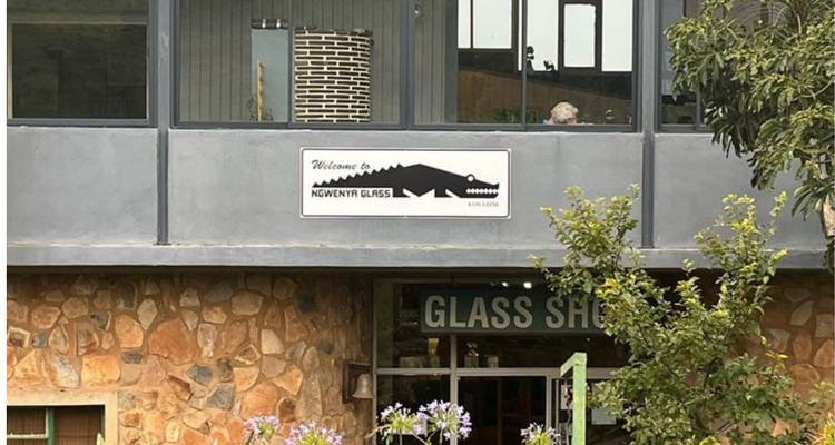 Entrada de la tienda Ngwenya Glass con paredes de piedra, señalización y vegetación