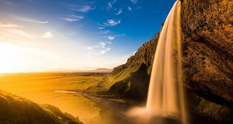 Golden-hour view of Seljalandsfoss waterfall plunging beside glowing plains