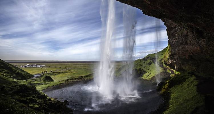 Daytime view from behind Seljalandsfoss with water streaks and vast plains beyond