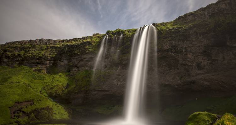 Full view of Seljalandsfoss dropping from green cliff under partly cloudy sky