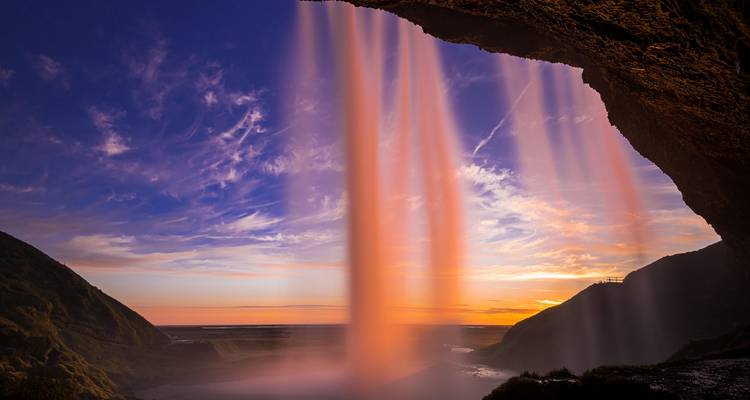 Seljalandsfoss waterfall glowing pink at vibrant sunset viewed from cave opening