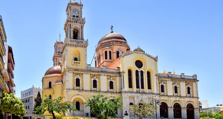 Large yellow-cream cathedral with twin bell towers and red domes set against a clear sky.