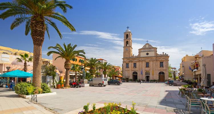 Sunny town square lined with palms, cafés and a modest stone church with bell tower.