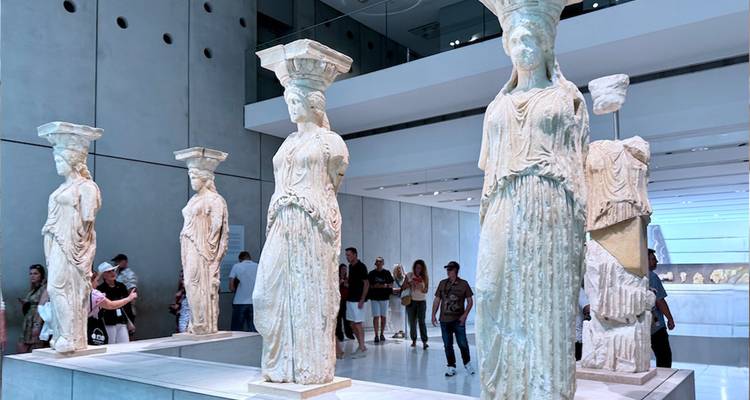 Des statues de Cariatides anciennes exposées dans une salle de musée moderne avec des visiteurs qui observent et prennent des photos.