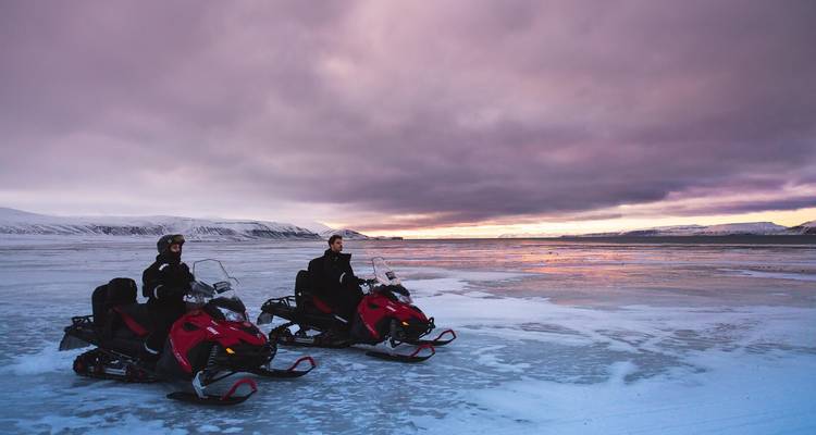 Two snowmobilers pause on frozen lake at colorful winter dusk