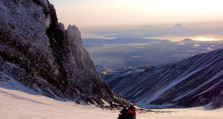 Climbers ascend snowy mountain valley overlooking distant coastline at sunrise