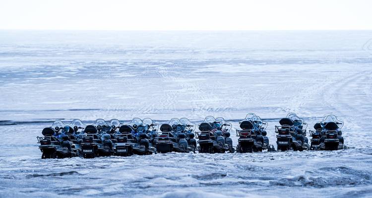 Long row of parked snowmobiles on icy expanse under bright overcast sky