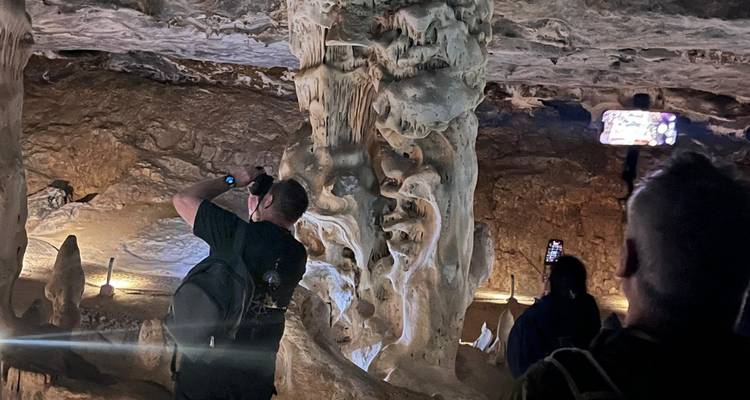 Los visitantes fotografían formaciones de piedra caliza dramáticas dentro de una cueva poco iluminada.