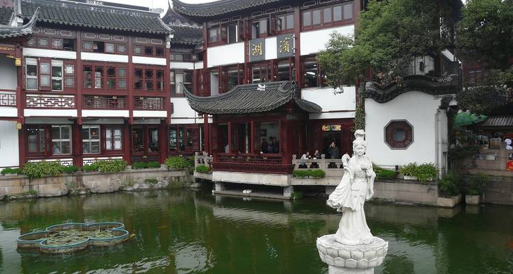 Traditional red-and-white courtyard buildings overlook a serene koi pond and statue.