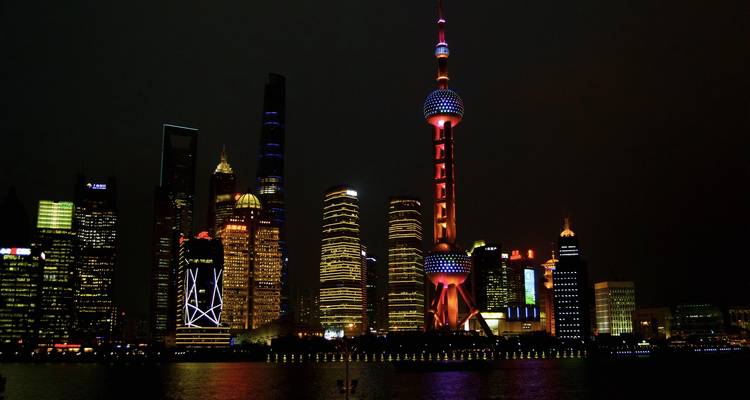 Shanghai skyline at night with the brightly lit Oriental Pearl Tower reflecting on water.