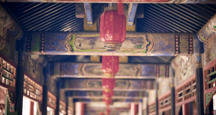 Ornate red lanterns hang in a richly painted wooden corridor of a historic building.