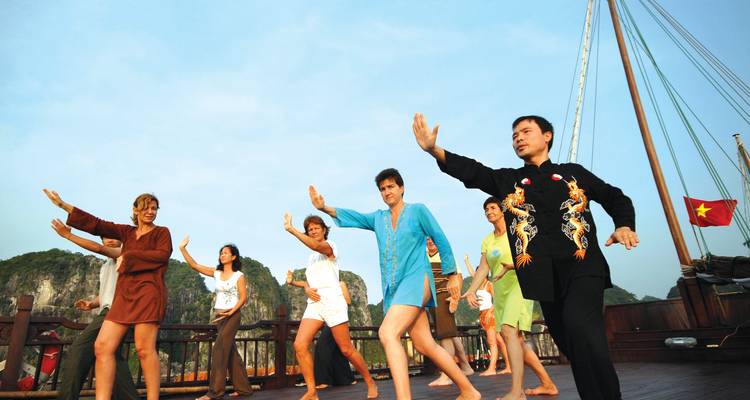 Reisende üben Tai Chi auf dem Deck einer hölzernen Dschunke inmitten der Kalksteininseln der Halong-Bucht.
