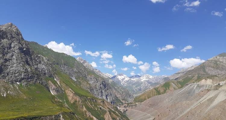 Valle amplio de picos grises y verdes dentados bajo nubes dispersas en Kirguistán