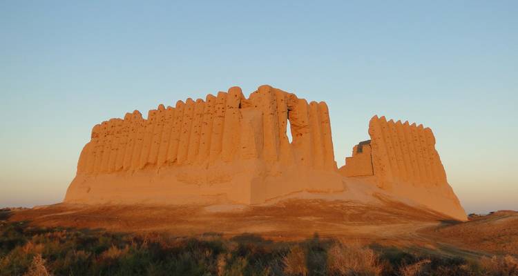 Imponentes muros de fortaleza de adobe iluminados por el sol de las antiguas ruinas de Merv elevándose desde la llanura desértica al atardecer
