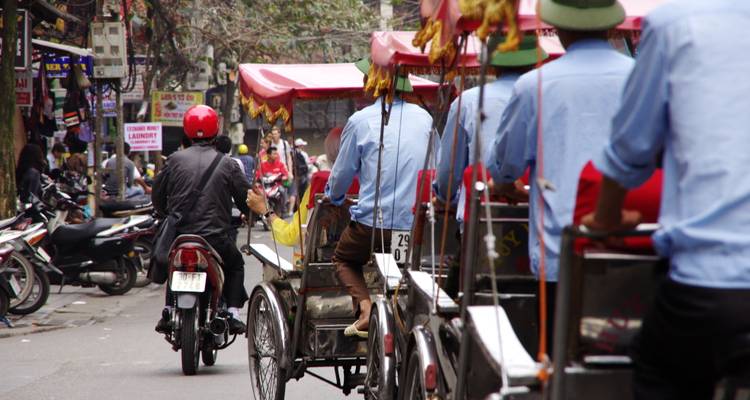 Geschäftige Straße in Hanoi, gefüllt mit Cyclos, Motorrädern und lebendigen Ladenschildern.