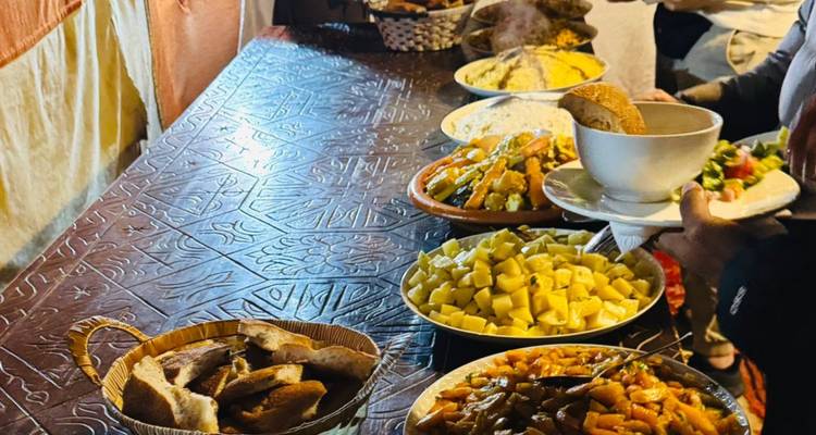 Buffet tradicional marroquí con pan, papas y tajines dentro de la carpa comedor del campamento