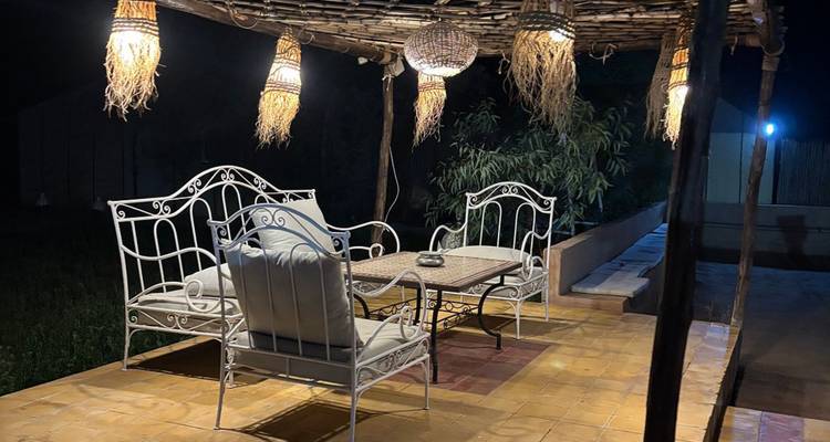 Acogedor salón exterior con muebles de hierro forjado y lámparas de linterna que brillan por la noche en el campamento del desierto