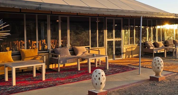 Lounge del campamento en el desierto con lona, alfombras y asientos bañados por la cálida luz del atardecer