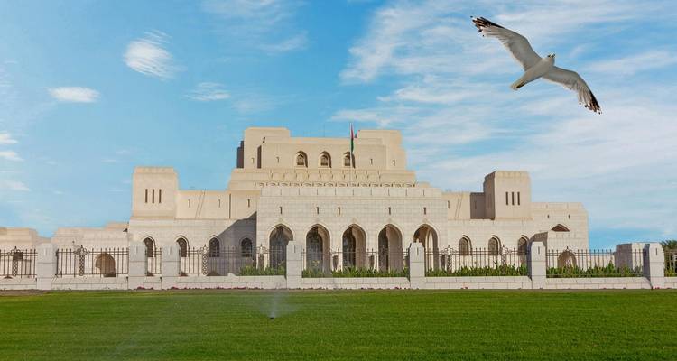 La Maison de l'Opéra royale en marbre blanc de Mascate contre un ciel bleu avec une mouette qui s'envole haut dans les airs
